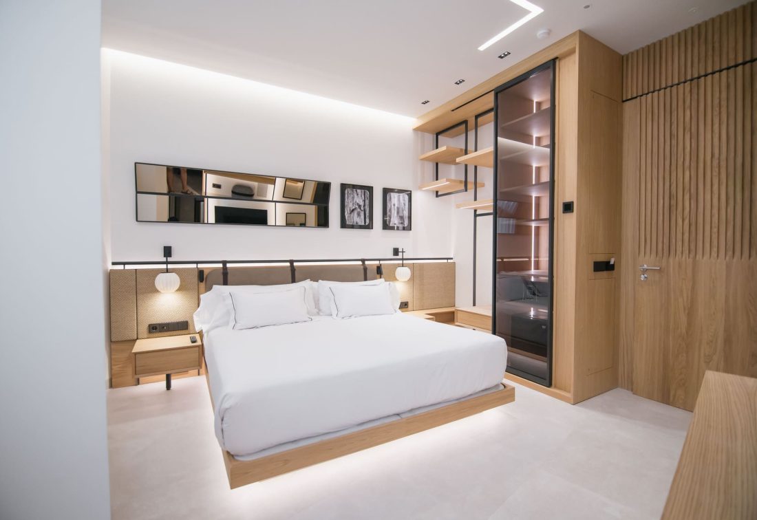 Habitación de hotel moderna con cama grande, cabecera acolchada y armario de madera