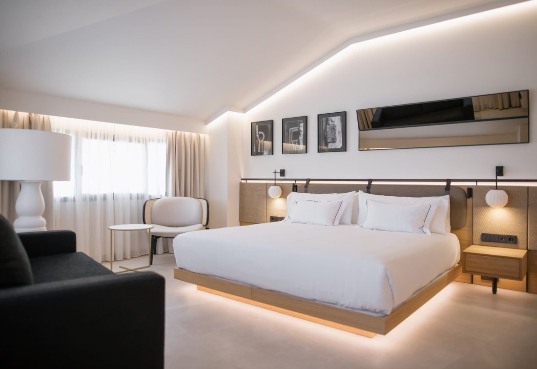 Habitación de hotel moderna con cama amplia, cabecero acolchado y iluminación ambiental.