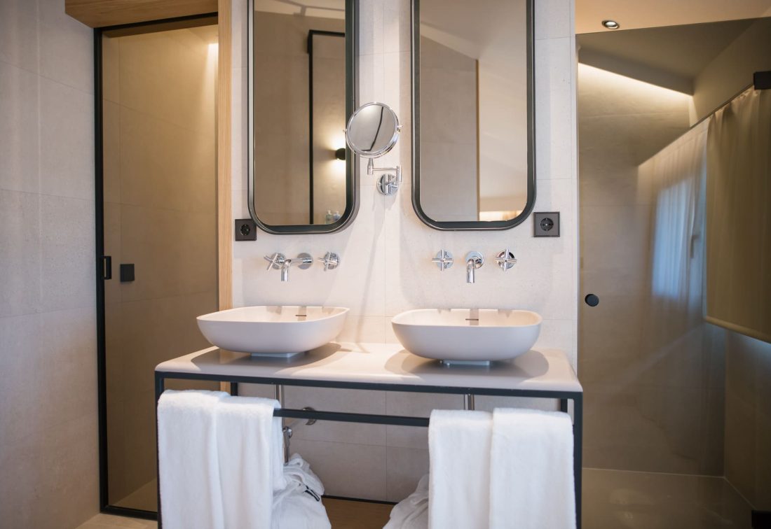 Lavabos dobles en baño de hotel con espejos ovalados y toallas blancas