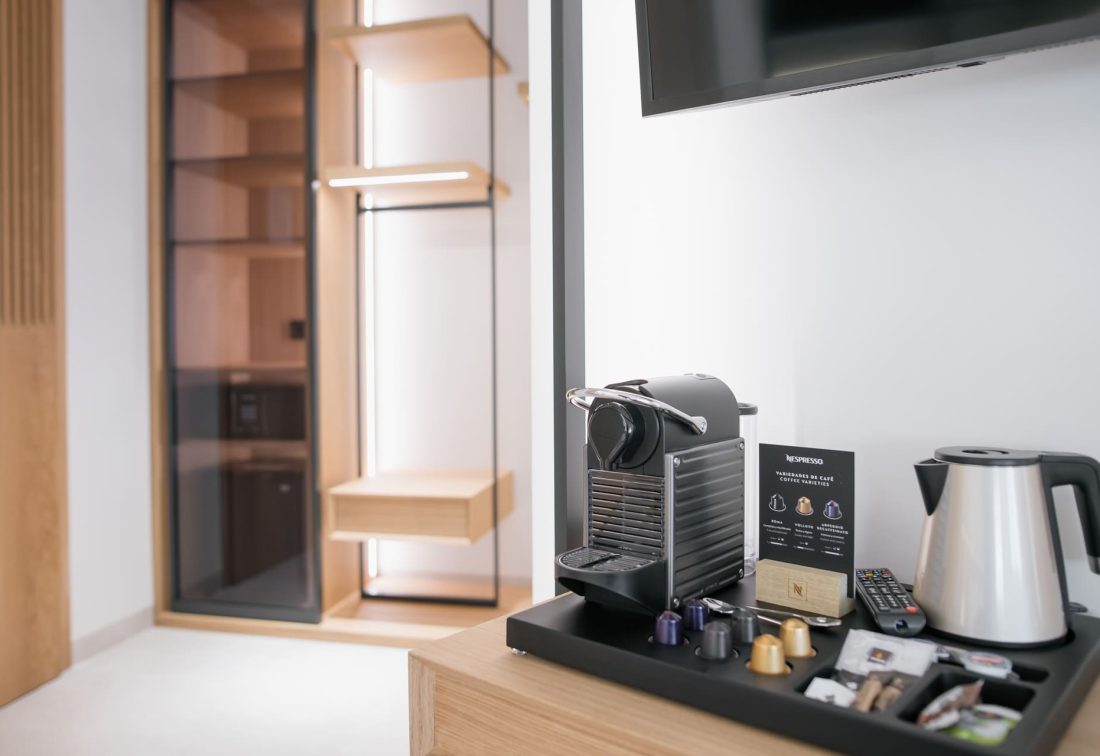 Máquina de café Nespresso y hervidor en habitación; vestidor de madera al fondo.