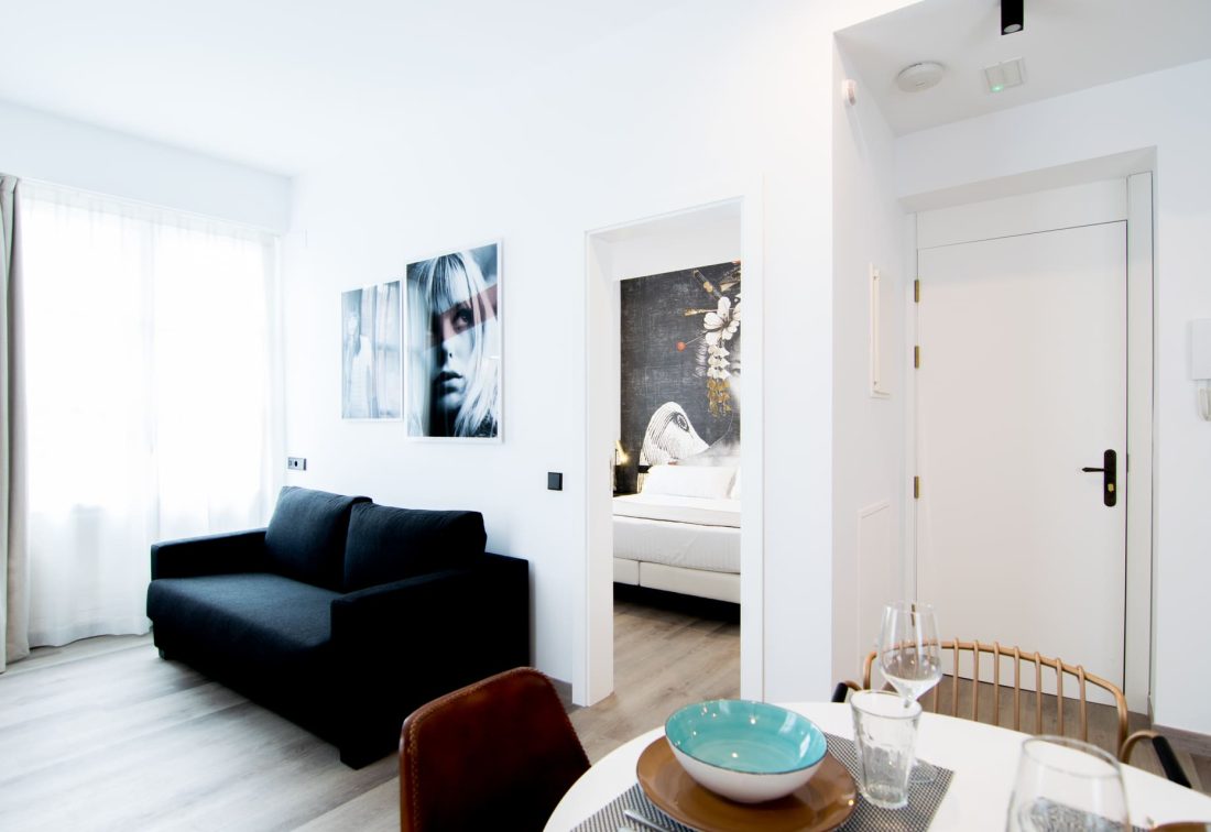 Sala de estar de suite de hotel con sofá negro, comedor y acceso al dormitorio