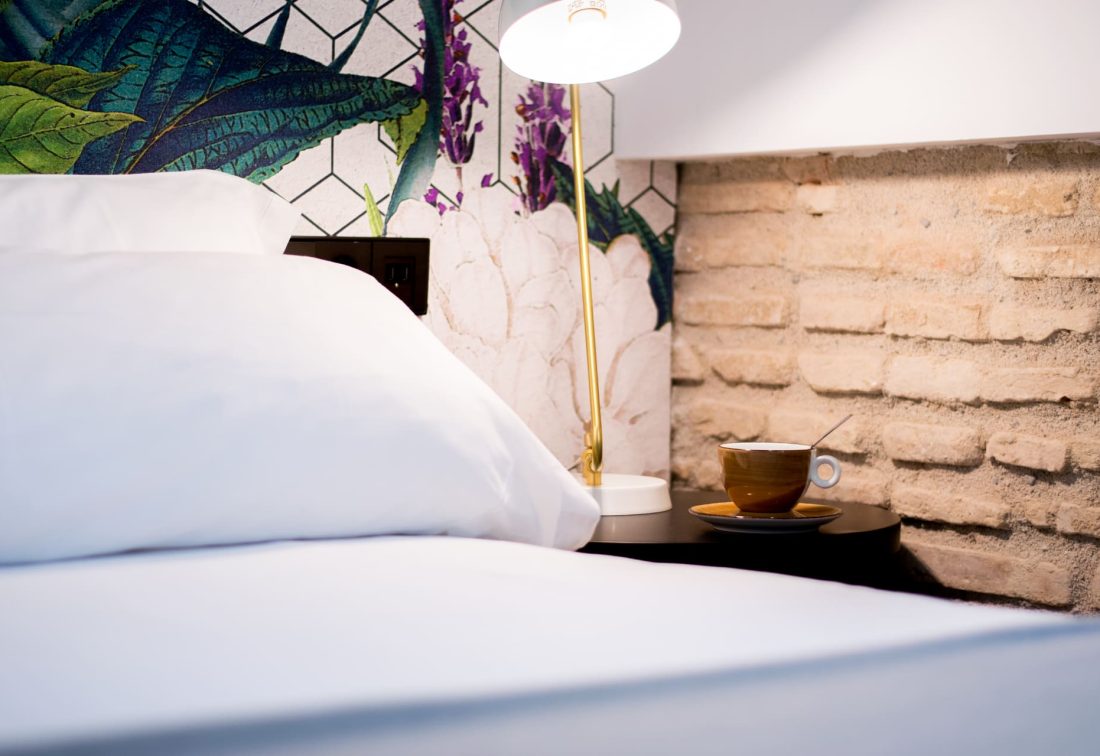 Cama con sábanas blancas junto a lámpara y taza de café en mesita