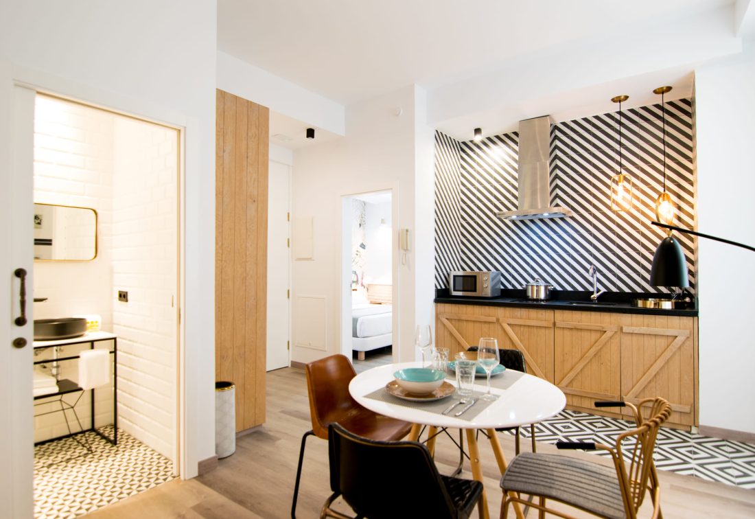 Cocina y comedor de apartamento en hotel, con mesa redonda blanca, sillas variadas y salpicadero a rayas blanco y negro.