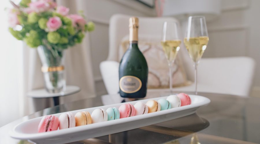 Macarons de colores en bandeja junto a botella de champán y copas, con ramo de rosas